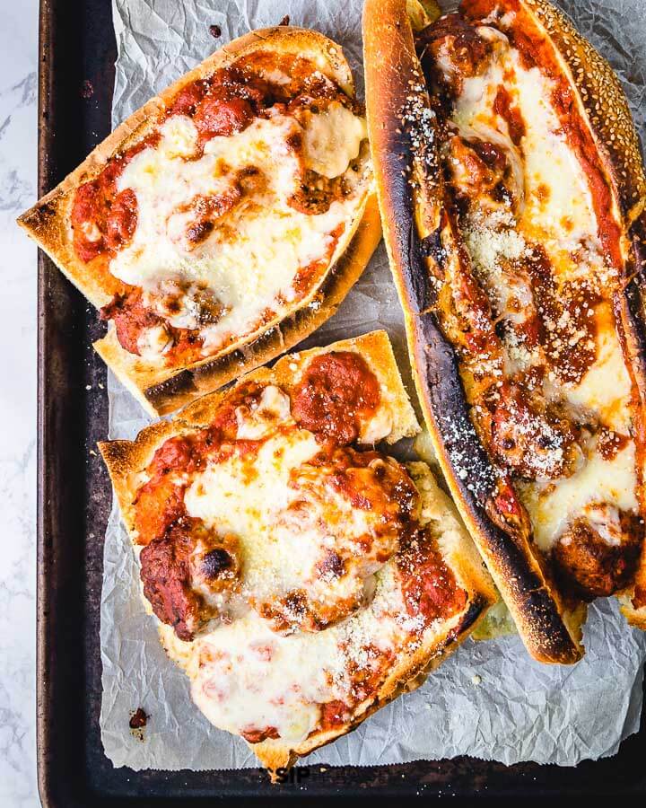 Three meatball subs in a sheet pan lined with parchment paper.