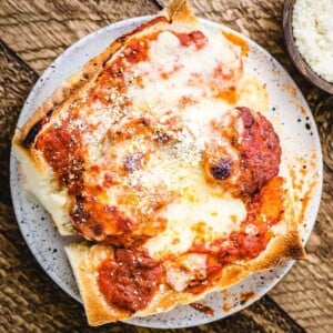 Meatball parm hero in white plate on wood table.