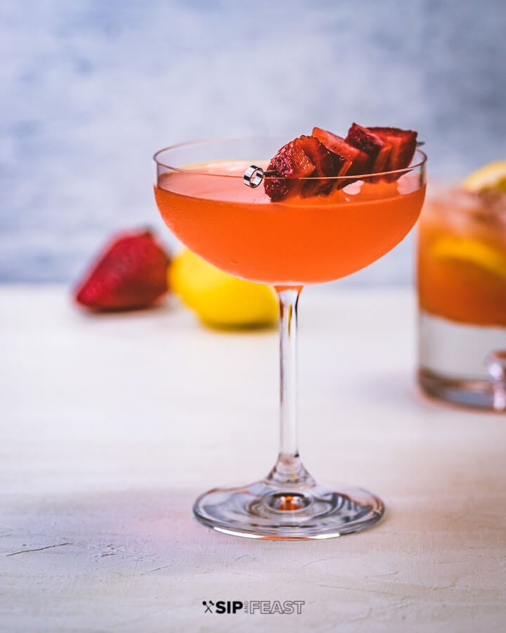 A coupe glass with strawberry lemonade vodka cocktail, with strawberries and lemons.