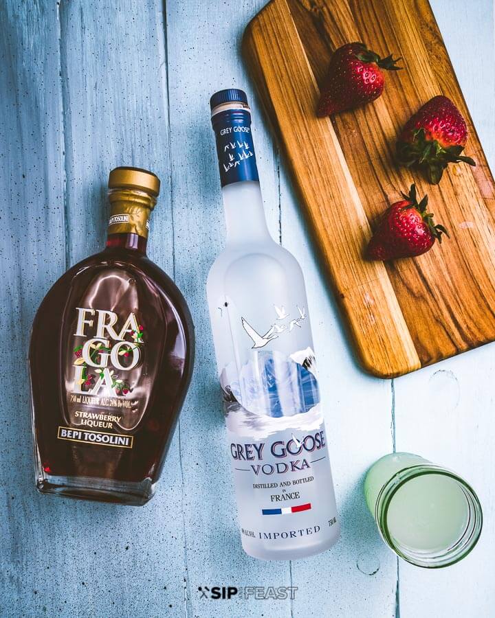 Strawberry liqueur, vodka, lemonade and strawberries on a cutting board.