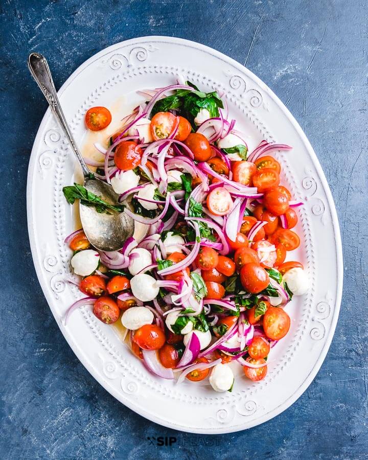 Tomato, basil and mozzarella salad in white platter on blue background.