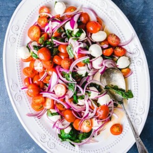 Tomato mozzarella salad in white plate on blue background.