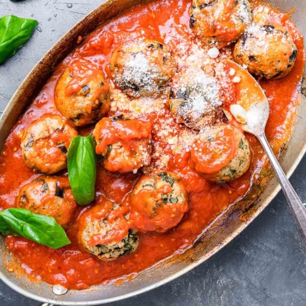Eggplant meatballs in oval pan sprinkled with Pecorino Romano and basil leaves.