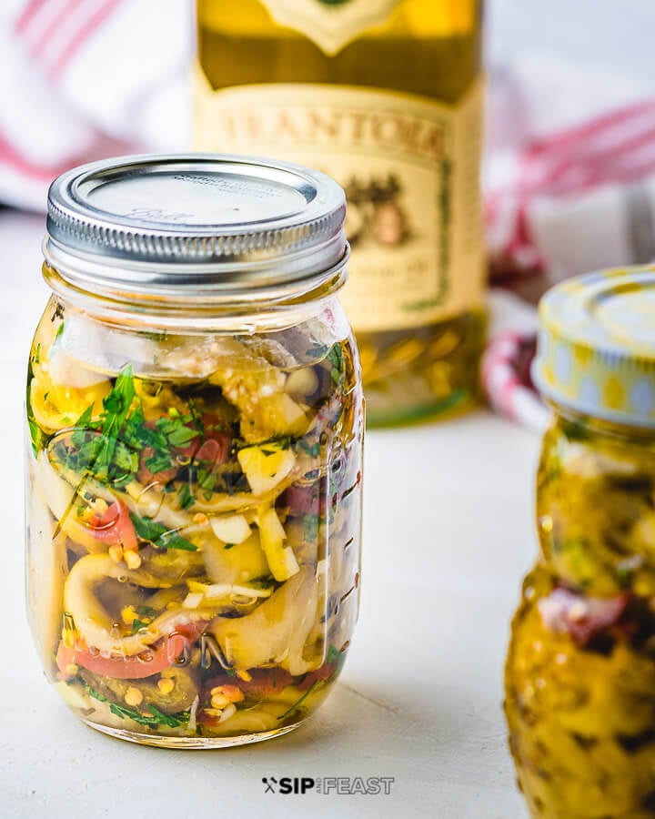 Italian Pickled Eggplant - sipandfeast.com #pickledeggplant #eggplant #italianrecipes Jar of Italian pickled eggplant with olive oil container in background.