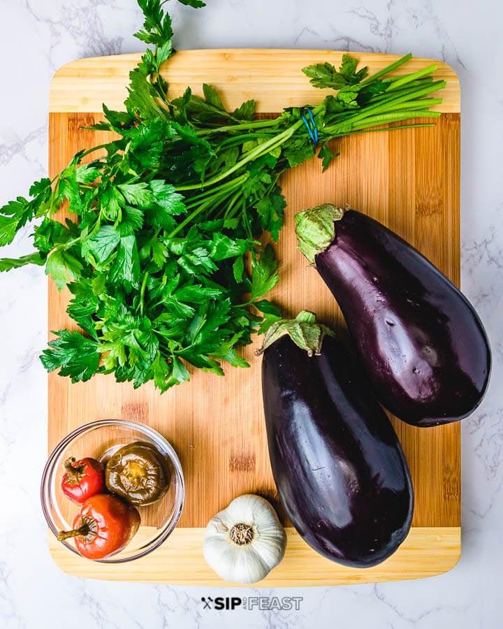 Italian Pickled Eggplant - sipandfeast.com #pickledeggplant #eggplant #italianrecipes Ingredients shown: parsley, cherry peppers, garlic and 2 eggplants on cutting board.