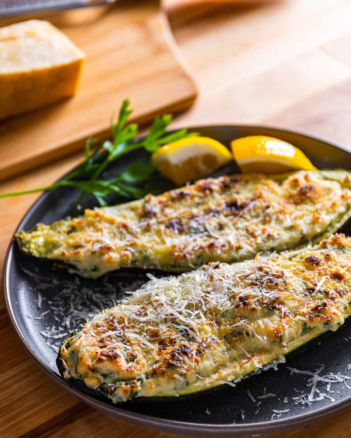 Two stuffed zucchini pieces in grey plate with lemon and parsley garnish.