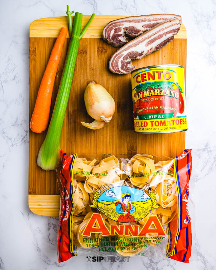 Ingredients on cutting board: carrot, celery, onion, pancetta, canned plum tomatoes and dried pappardelle pasta.