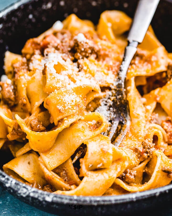 Pappardelle bolognese in black bowl with Parmigiano Reggiano on top.