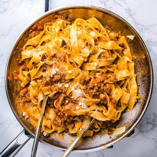 Pappardelle bolognese in large pan with tongs.