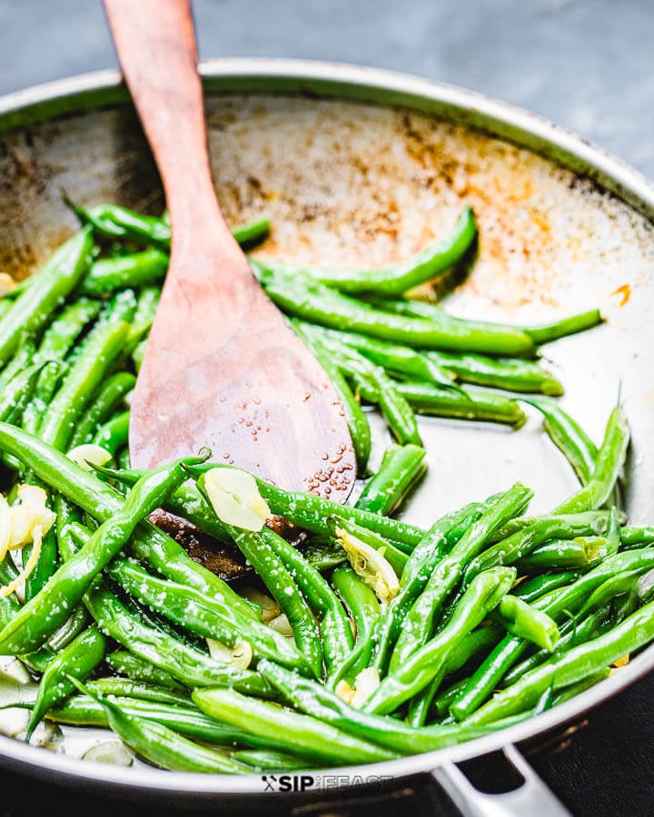 String beans with garlic and oil in pan on blue background.