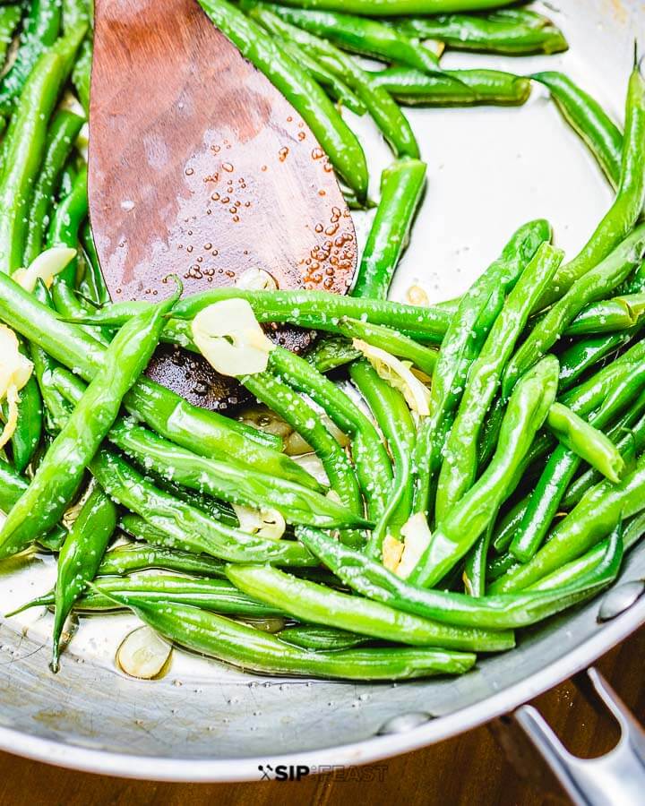 Sauteed garlic string beans in pan with wooden spoon.