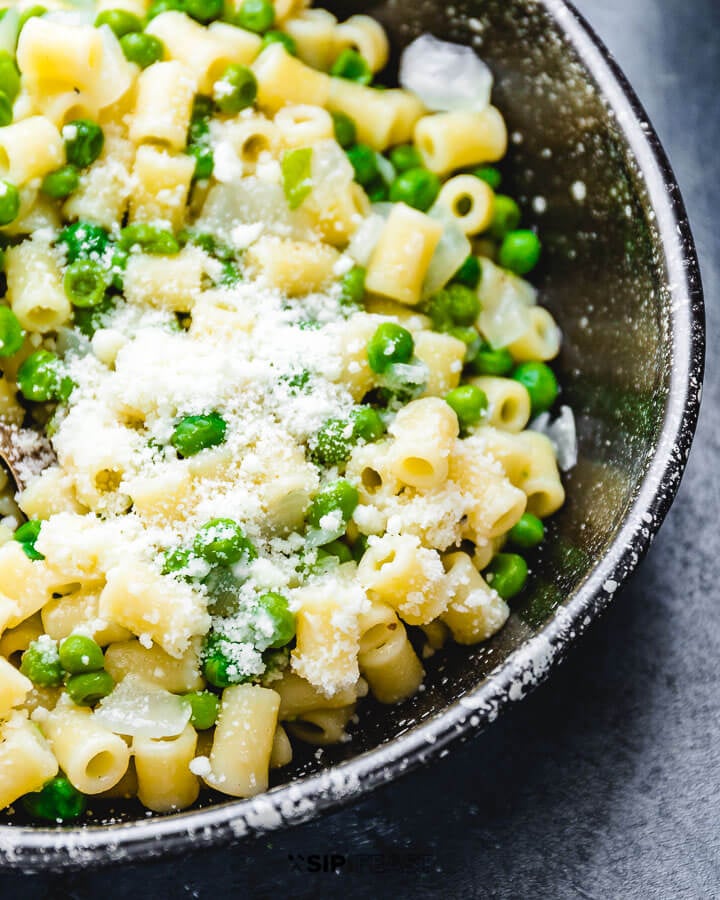 Pasta and peas in black plate with sprinkled cheese.