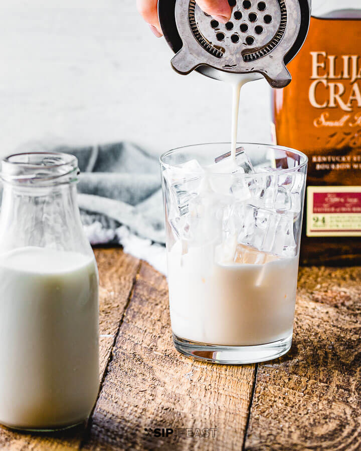 Pouring the milk punch mixture into a glass filled with ice.