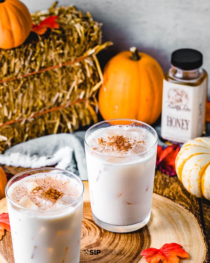 Two glasses of bourbon milk punch with pumpkins , honey, and a hay bale in the background. 