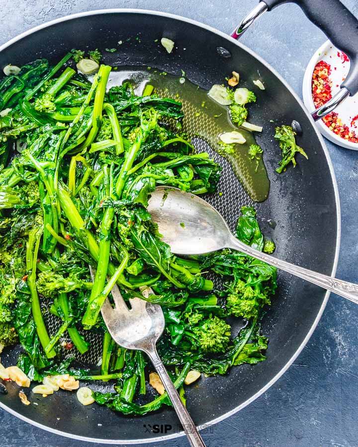 Sauteed broccoli rabe in pan on blue board.