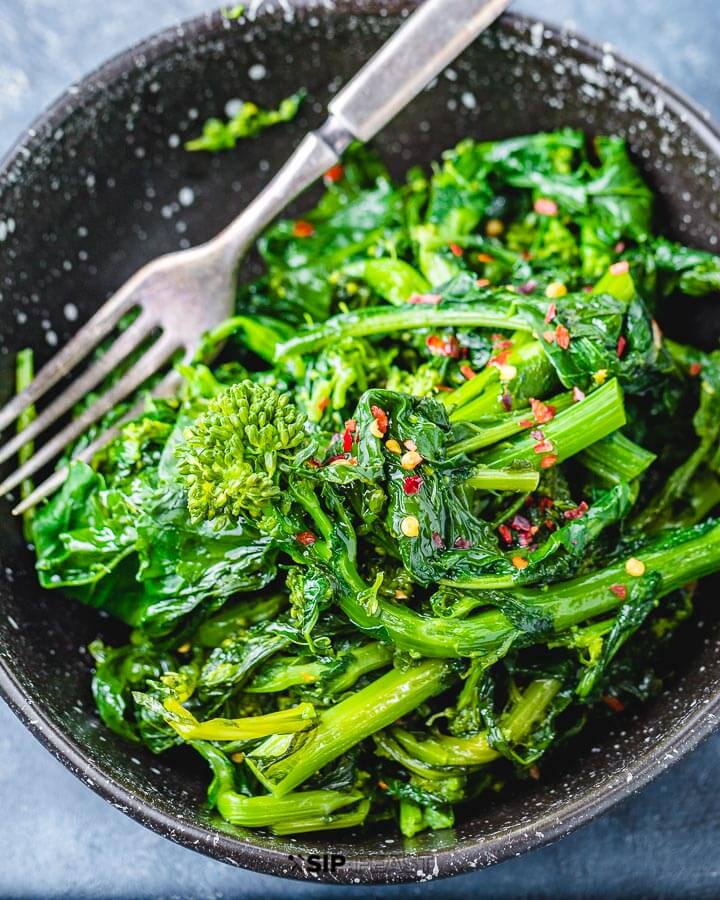 Black bowl with broccoli rabe on blue table.