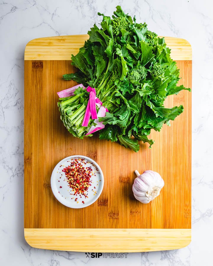 Ingredients on cutting board: One bunch of broccoli rabe, red pepper flakes, and head of garlic.