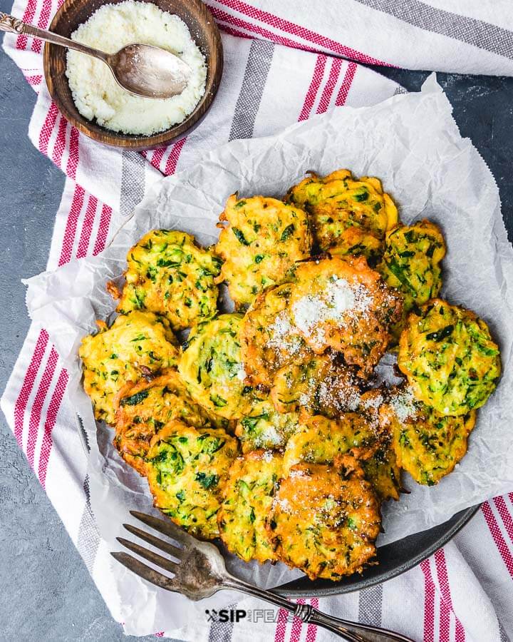 Plate of zucchini fritters on towels with bowl of cheese on the side.