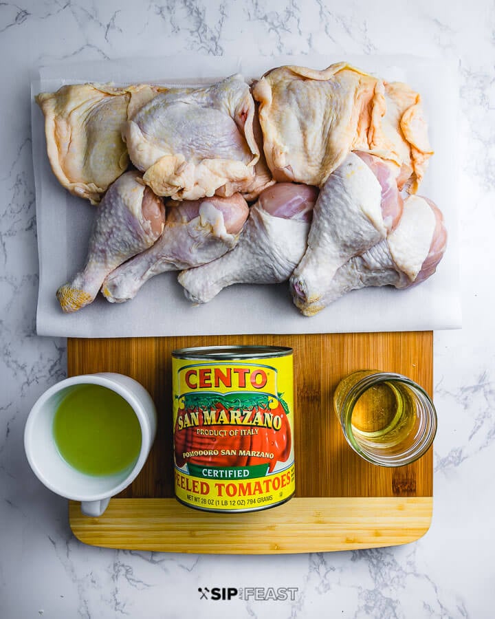 Ingredients on cutting board: chicken pieces, chicken stock, canned plum tomatoes, and white wine.