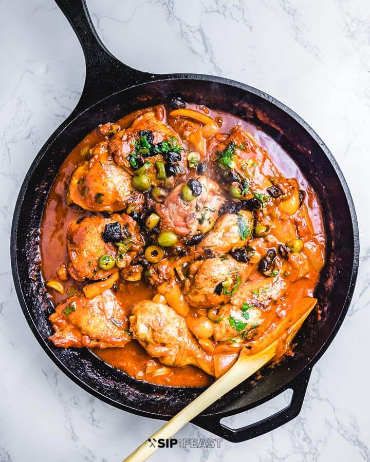 Chicken Cacciatore in cast iron pan on white marble table. 