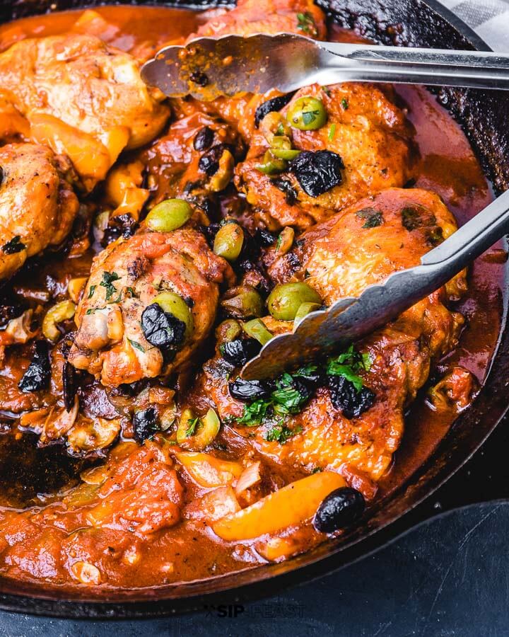 Chicken cacciatore in pan with metal tongs.