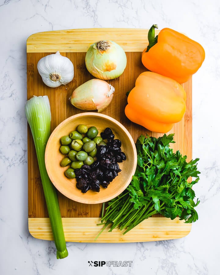 Ingredients shown on cutting board: garlic, onions, bell peppers, celery, olives, parsley.