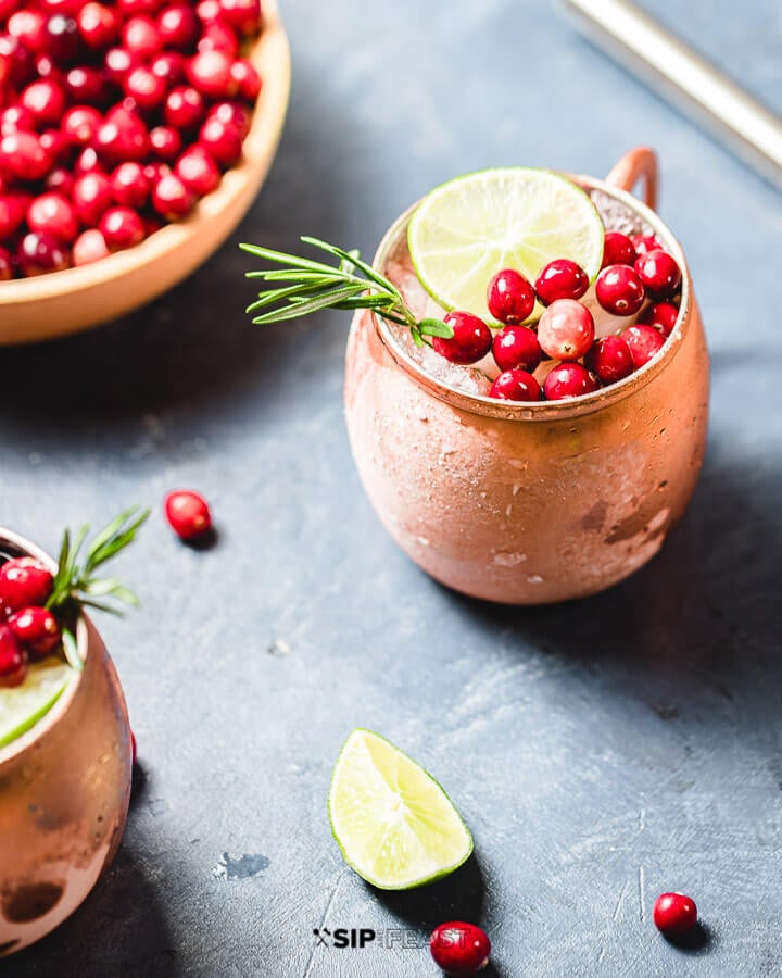 Bowl of cranberries and two copper mugs filled with the Cranberry Moscow Mule.