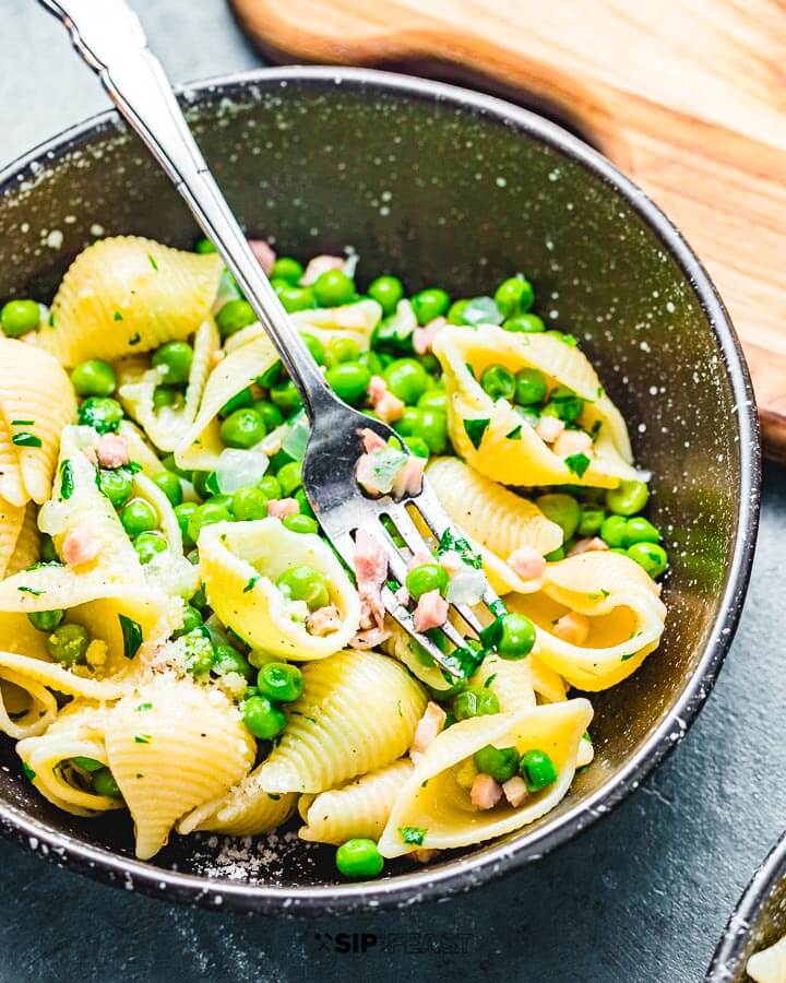 Pasta shells with pancetta and peas in black bowl.