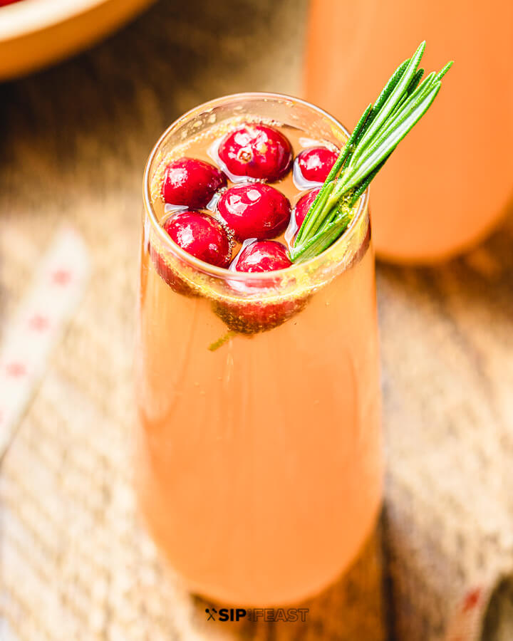 Closeup shot of Cranberry Mimosa with cranberries and rosemary.