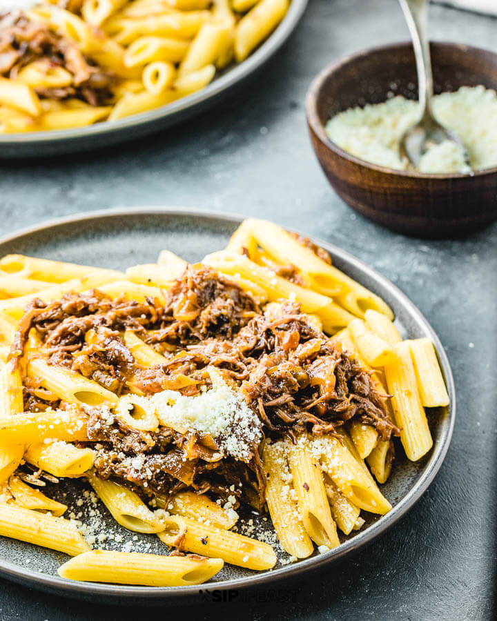 Pasta Alla Genovese in grey plate with bowl of grated cheese in background.