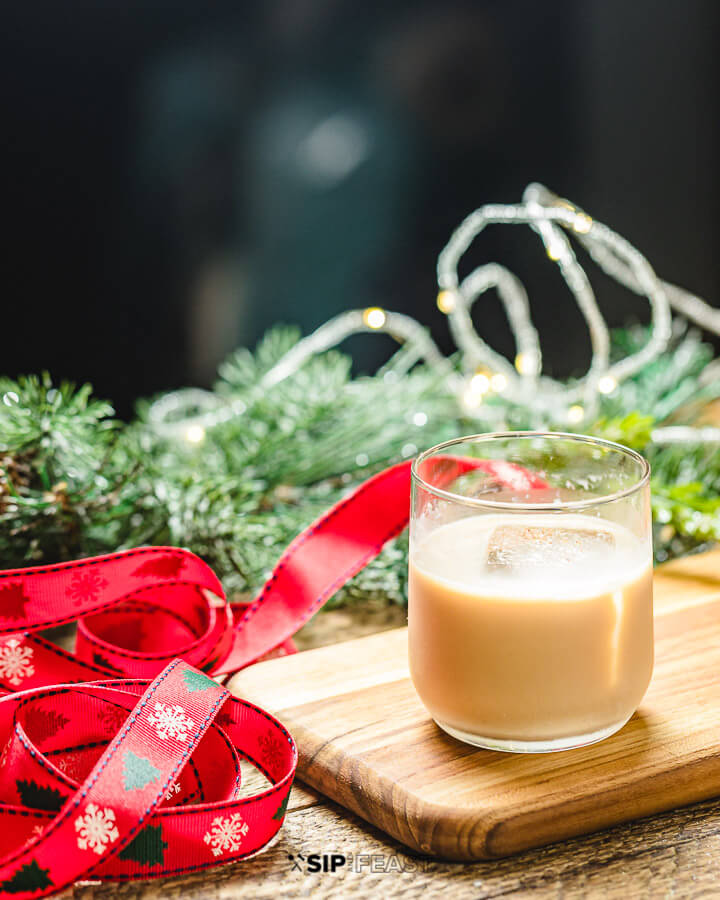 Glass of eggnog white Russian with ribbon, pine leaves and lights.