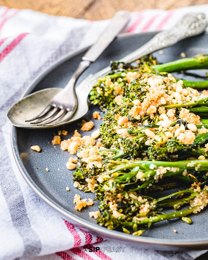 Grey plate with roasted baby broccoli and toasted pine nuts.