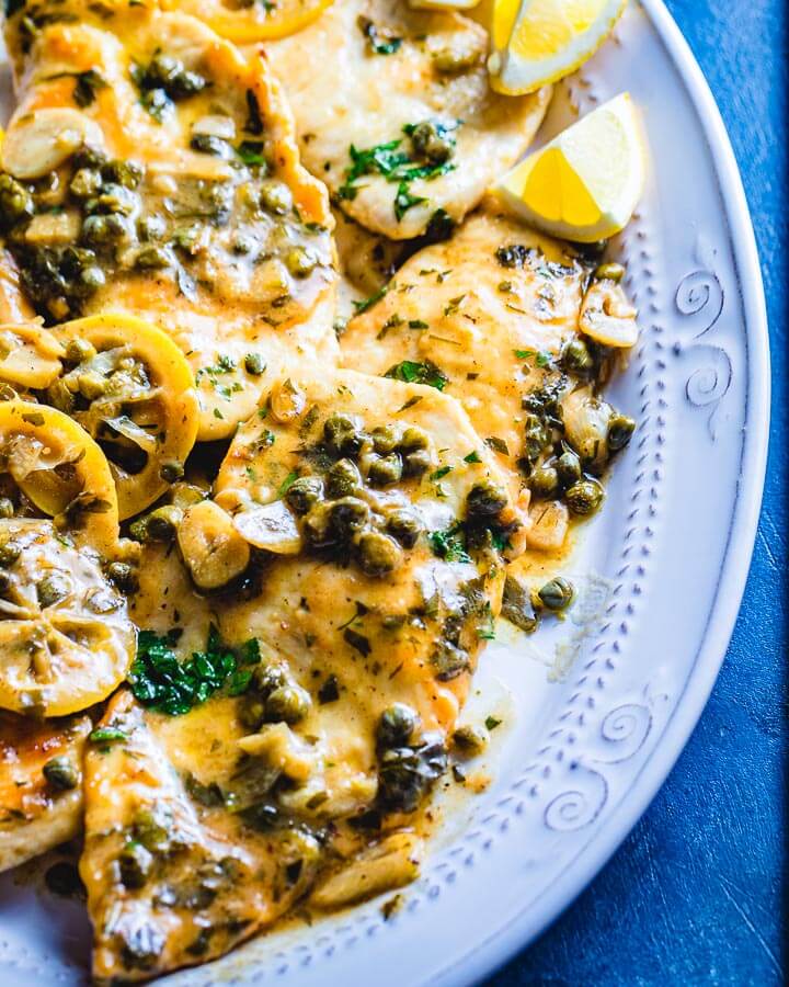 Chicken Piccata in white serving plate on blue board.