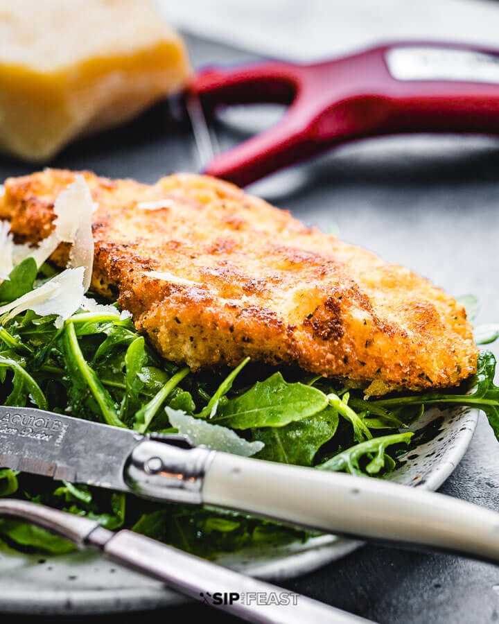 Italian chicken cutlet on top of arugula salad in white plate. 