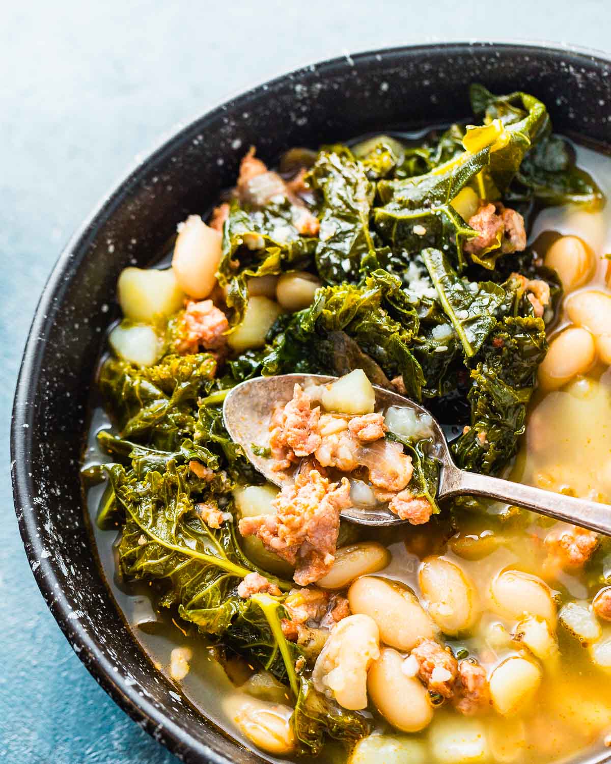 Black bowl of soup with mostly kale showing in bowl.