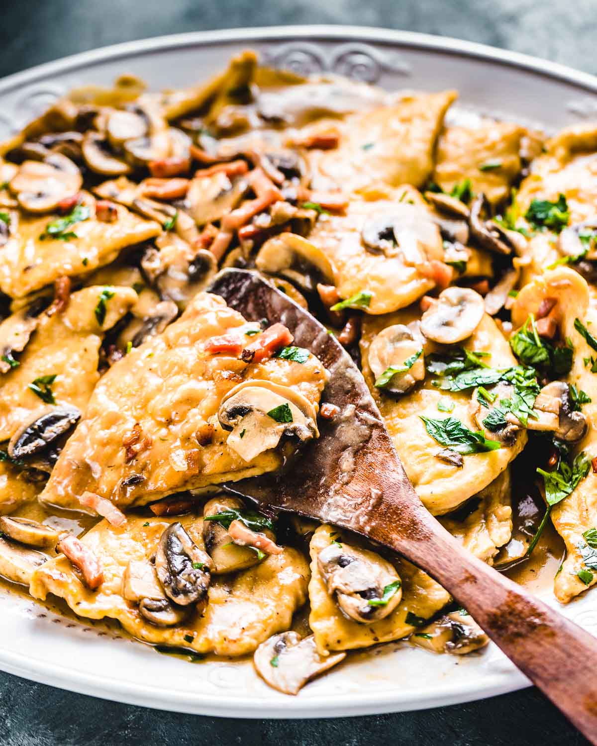 Spatula holding piece of finished chicken marsala over large platter.