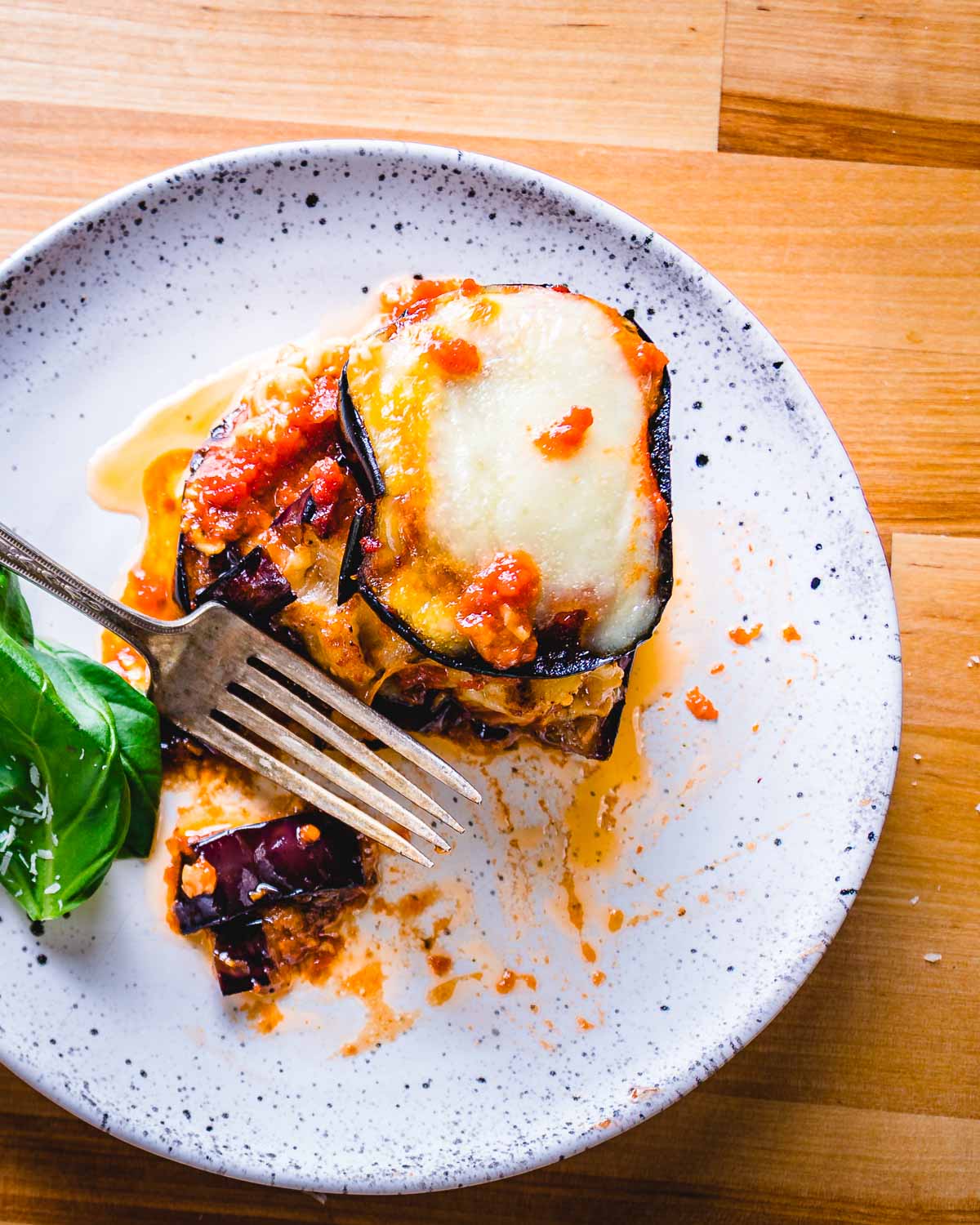 One serving of eggplant parm in white plate with fork on table.