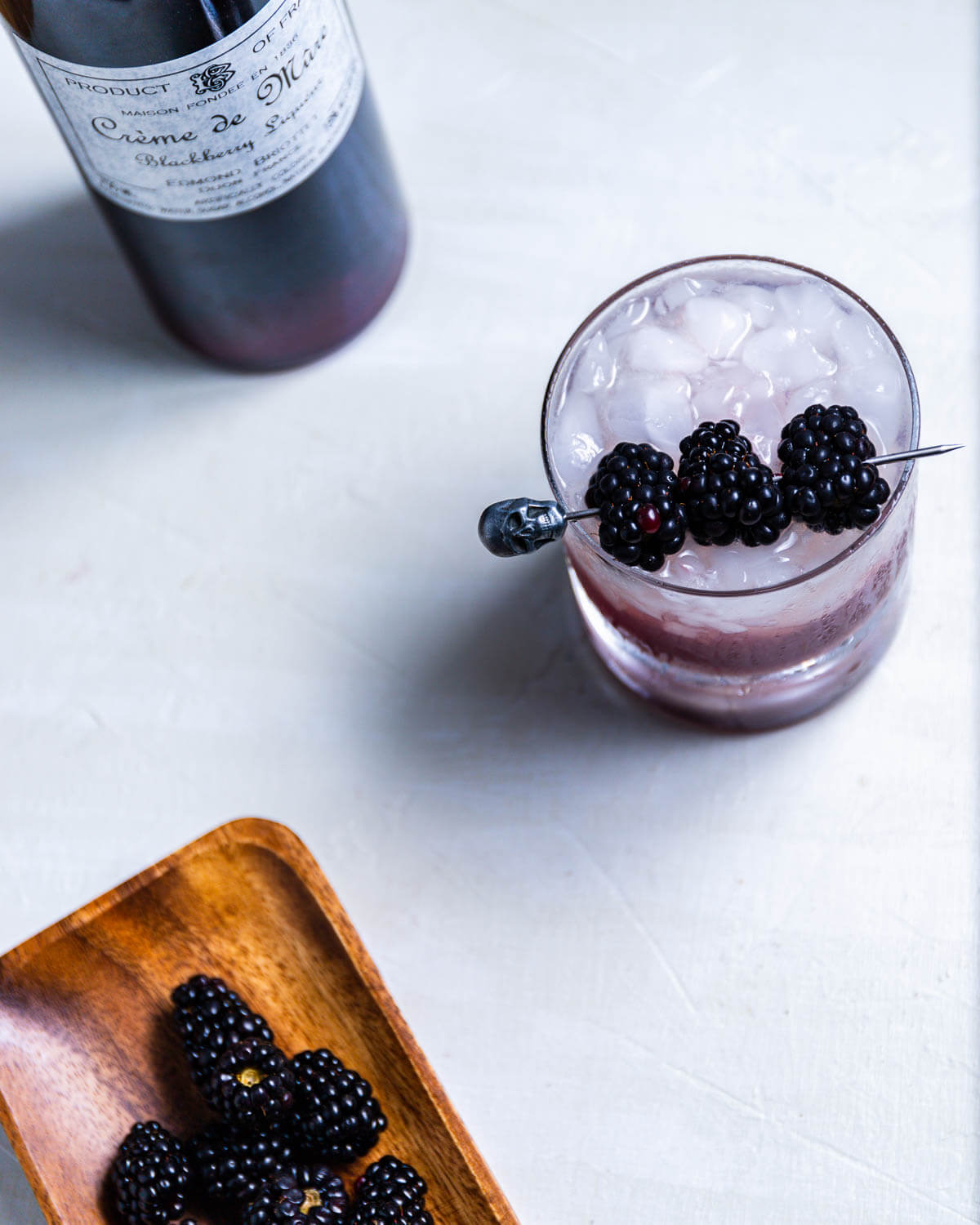 Overhead shot of Blackberry Bramble with Creme de Mure bottle and plate of blackberries.