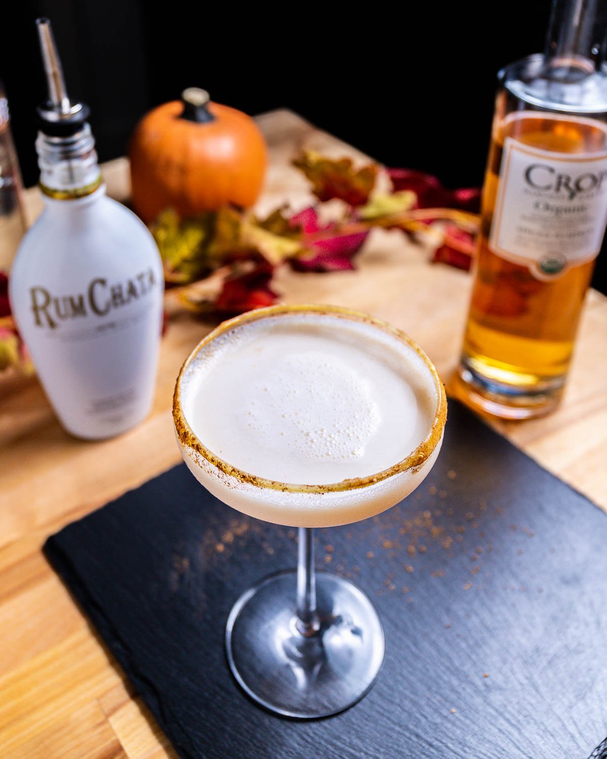 Pumpkin spice martini on table along with bottle of Rum Chata and pumpkin vodka.