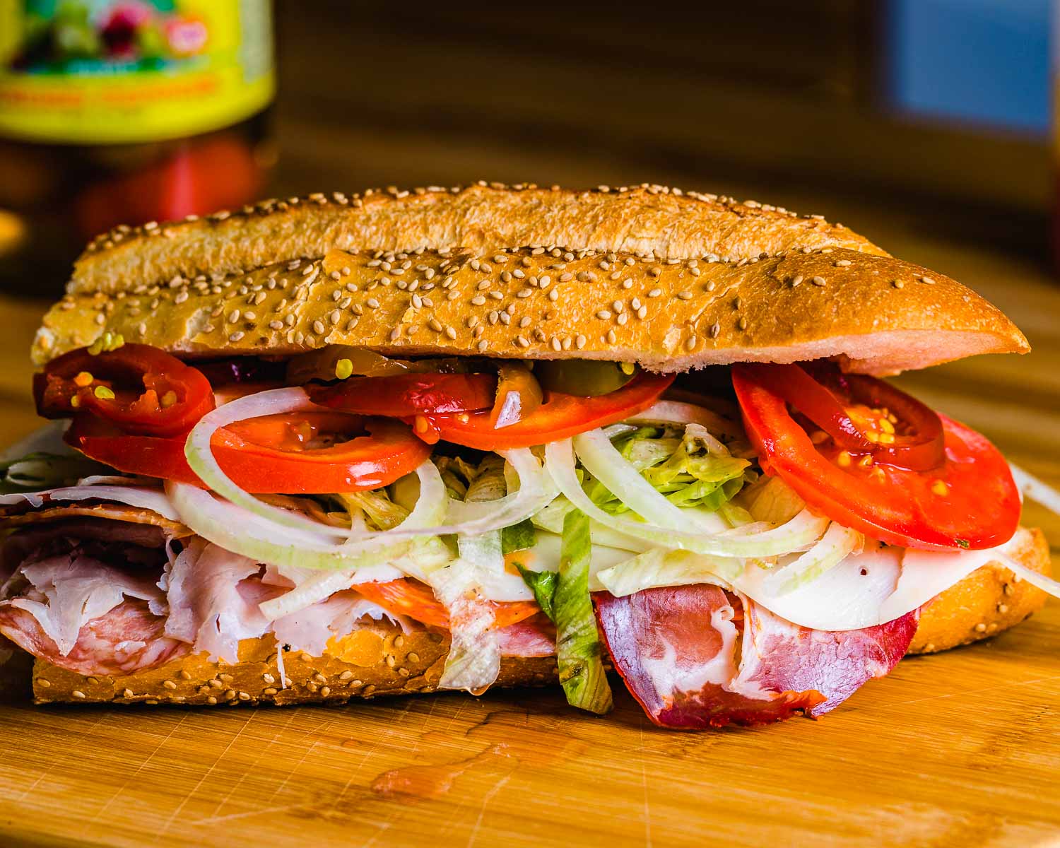 Italian sub on seeded roll with lettuce, tomato, cherry peppers, and onions showing.