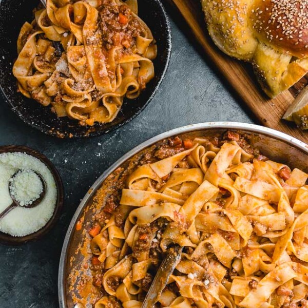 Overhead shot of bowl of pasta bolognese, large pan, and loaf of bread.