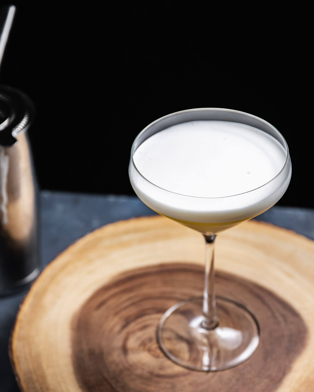 Cocktail in coupe glass on round wooden board.