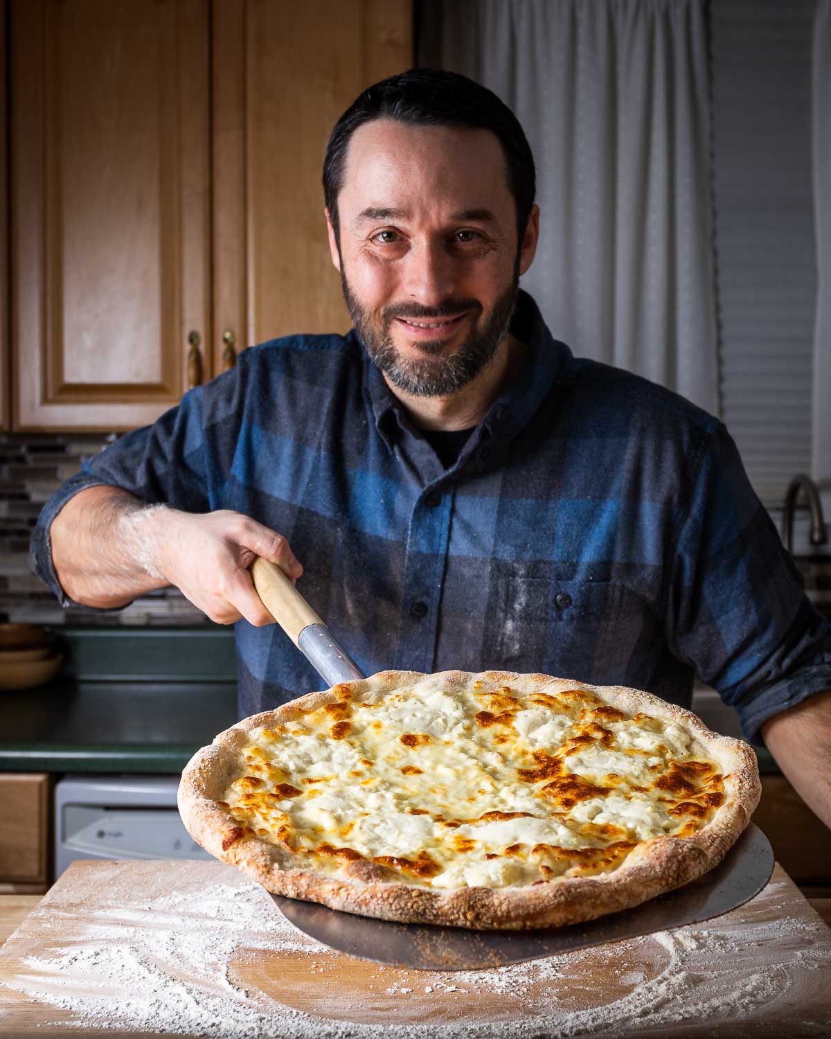 Jim holding a full white pizza on peel.