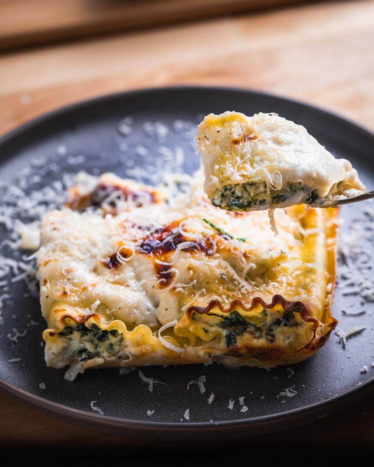 Cut piece of spinach lasagna roll up being held in fork.