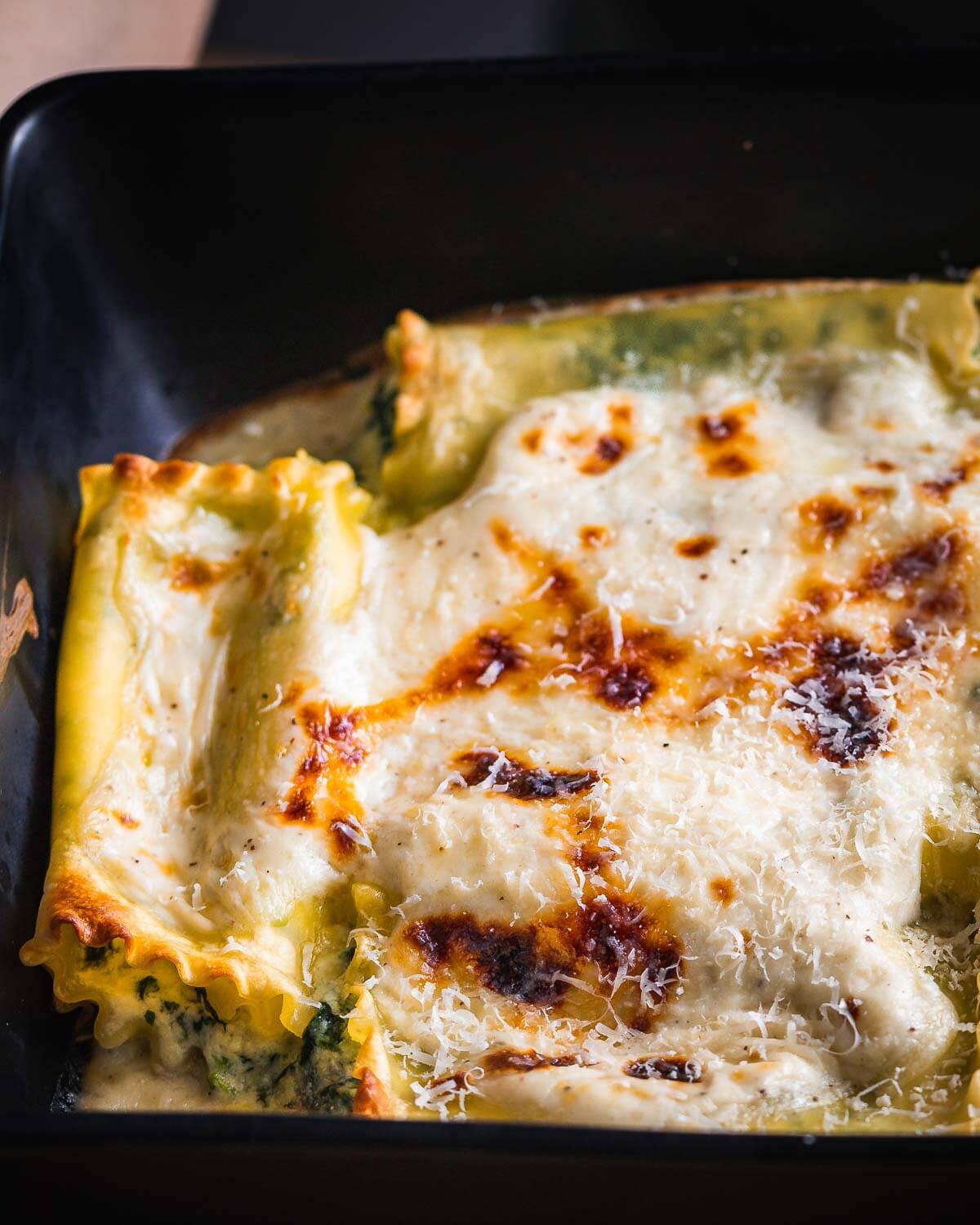 Spinach lasagna rolls with white sauce in black baking dish.