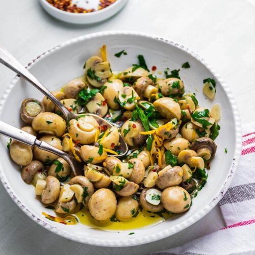 Marinated mushrooms in white bowl on white table.