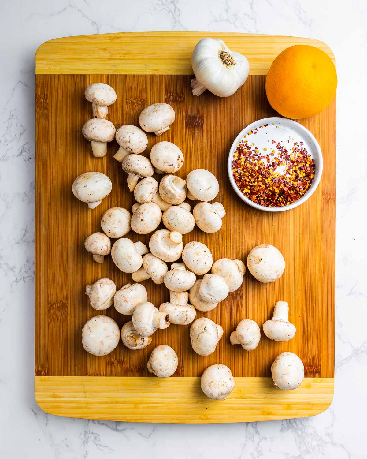 Ingredients shown: white button mushrooms, garlic, hot red pepper, and an orange on wood cutting board.