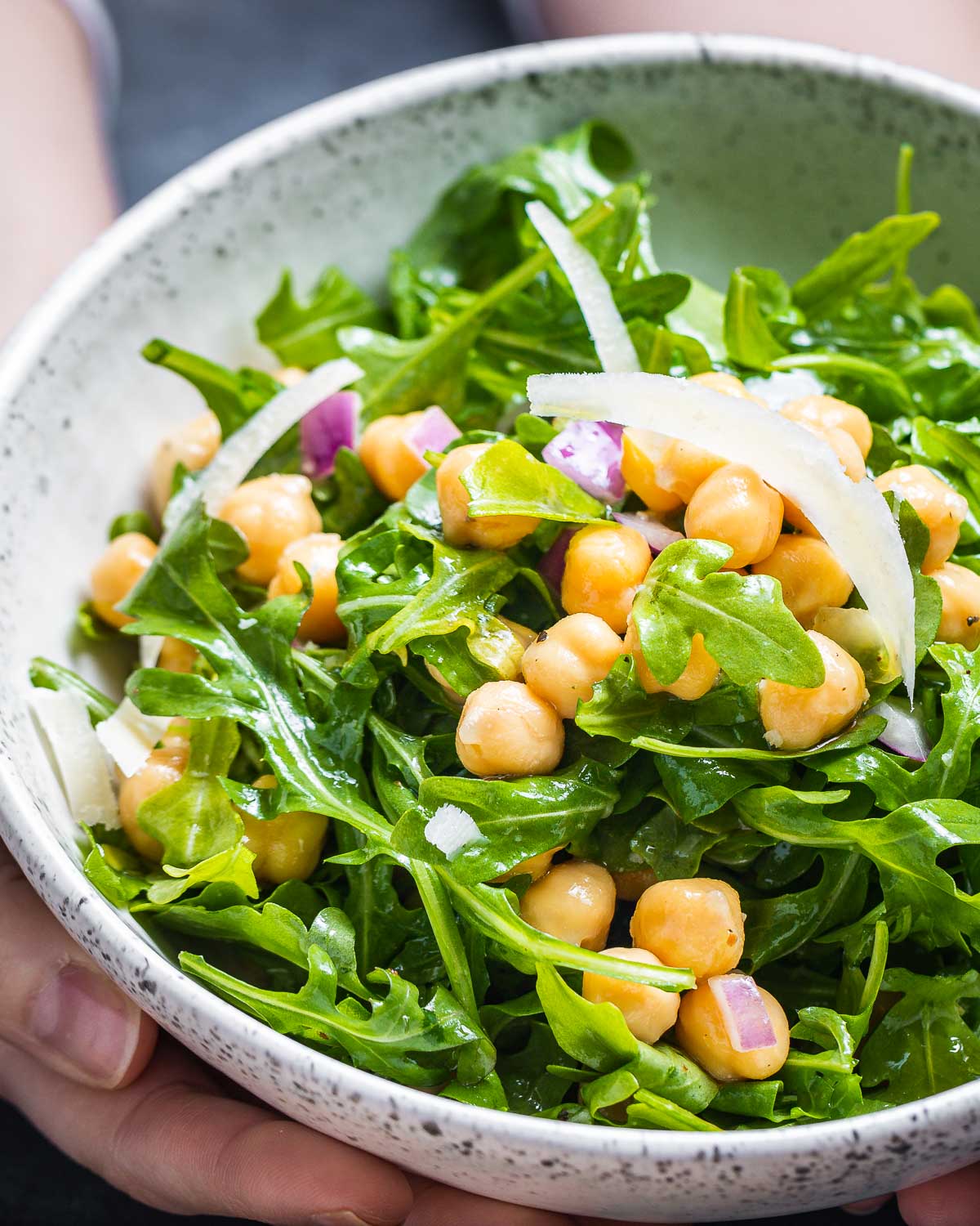 Arugula and chickpea salad being held in white bowl.