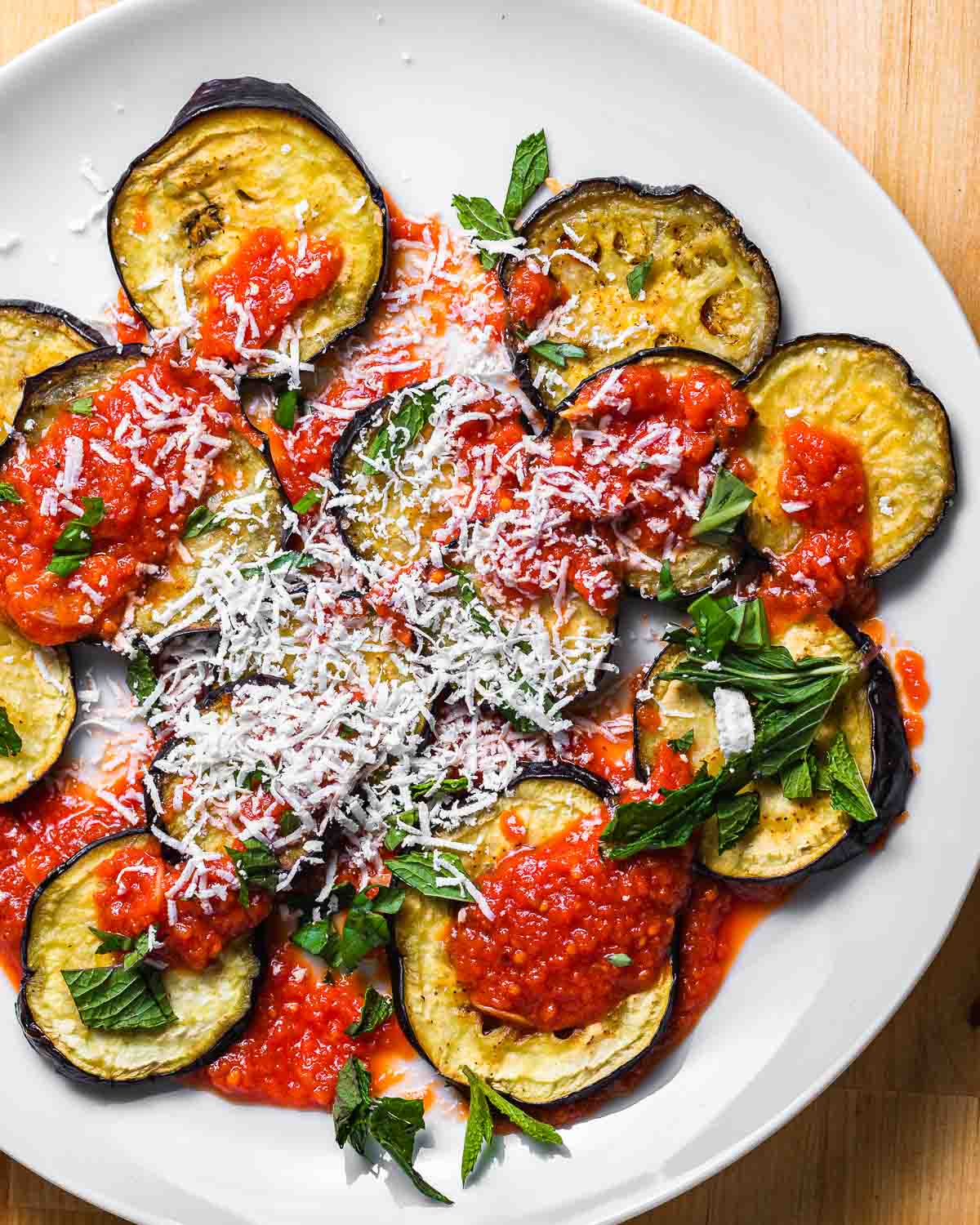 Round plate with eggplant discs, sauce, herbs, and cheese.