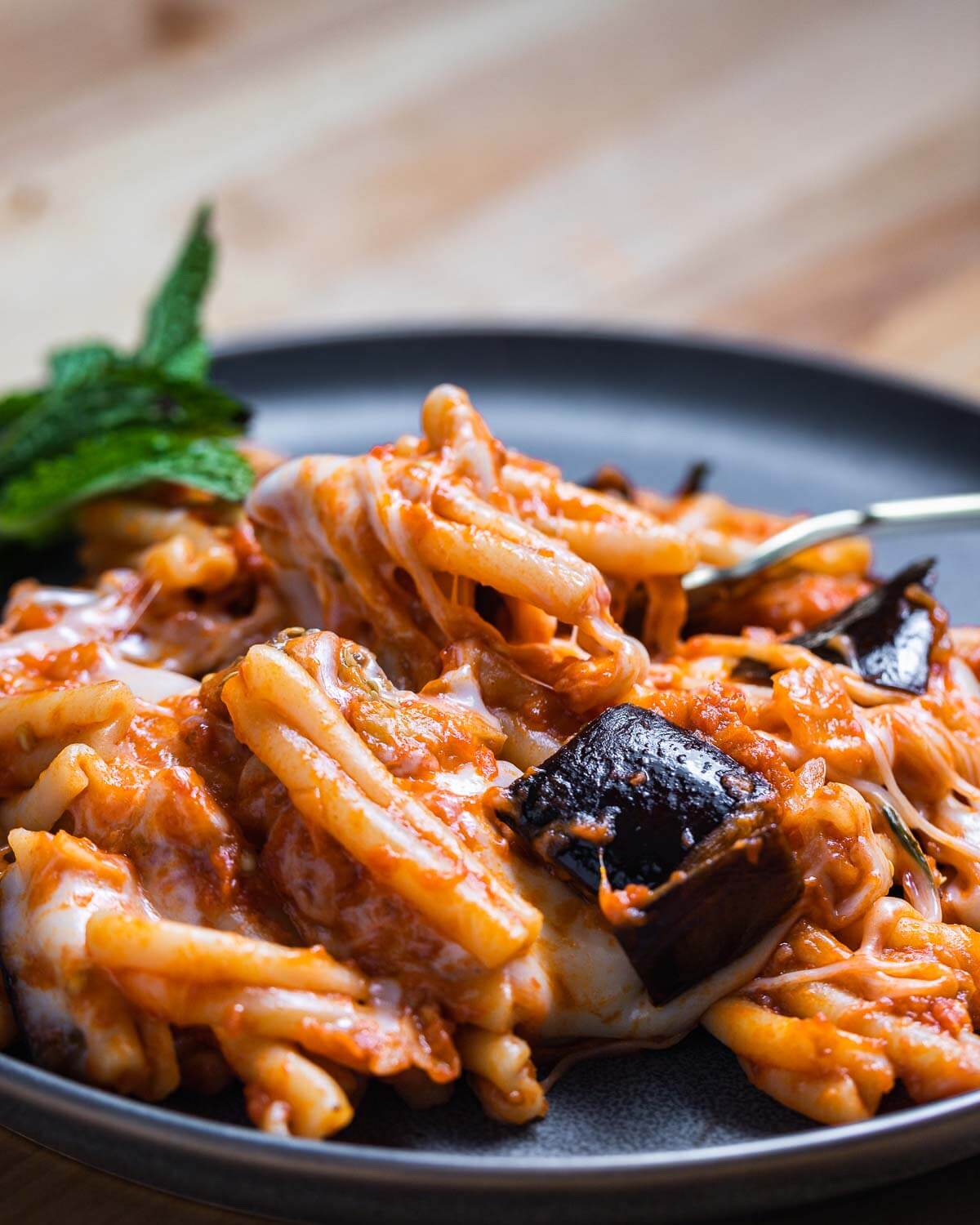 Grey plate with Pasta alla Siciliana with fork and mint garnish.